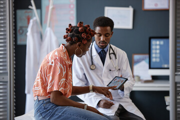 Side view of adult African American woman pointing at the screen during consultation with doctor in...