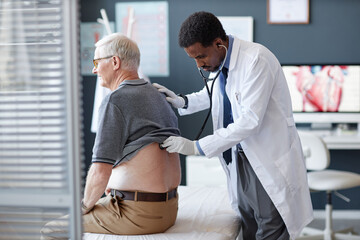 Side view of African American doctor using stethoscope and listening to heart and breathing while...