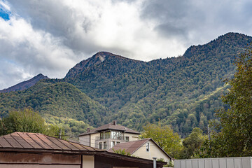Picturesque mountain resort landscape with low clouds on mountain peaks and low houses in foothill...