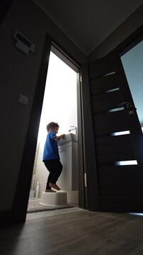 Toddler boy stands at the sink in the bathroom using a prop. Rear view of the kid paying with faucet and water. Low angle perspective. Vertical video.