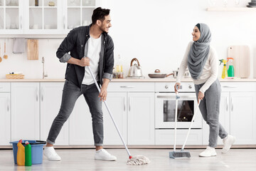 Loving middle-eastern family young husband and wife in hijab cleaning kitchen together, happy...
