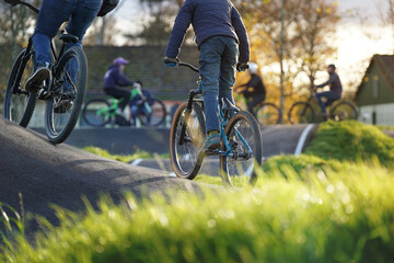 Children and teenagers riding bikes together on a pumptrack at a community park during autumn....