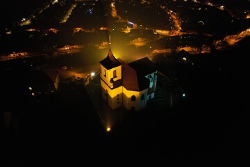 Aerial night view of an illuminated old church standing majestically on a hill, blending historical charm with the serene beauty of light and shadow in the evening	
