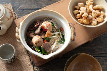 A bowl of boat noodles with various toppings, including meatball, pork, and crispy pork rind.