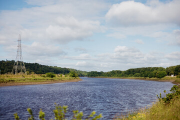 Newcastle UK: 5th July 2024: Newburn Riverside Park. River Tyne landscape with lush greenery and power lines under a partly cloudy sky