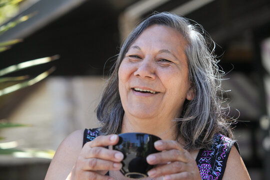 senior latin woman drinking coffee or tea outdoors on sunny summer day  