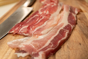 Raw Closeup of Slices of Bacon on a Wooden Cutting Board with a Stainless Steel Knife