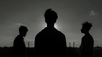 Silhouettes of three men against dramatic sky. Mysterious figures backlit by sunlight. Atmospheric scene with industrial backdrop. Moody cinematic style for film, music video, or poster.