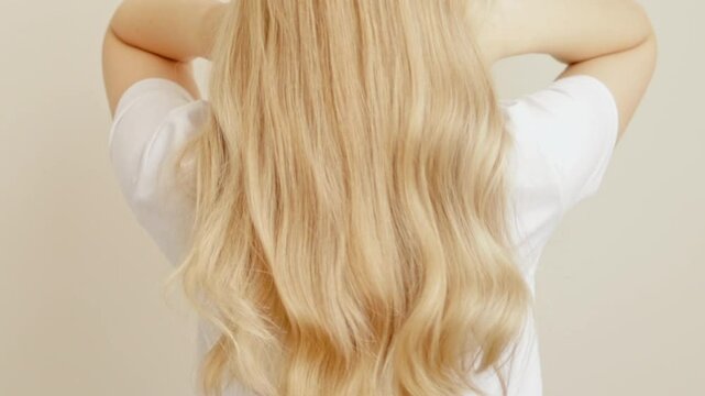 Blonde woman stands with her back throws long wavy hair. The concept of dyeing and hair extensions.