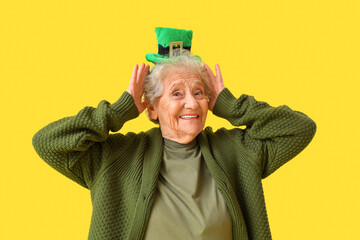 Happy senior woman with leprechaun hat on yellow background. St. Patrick's Day celebration