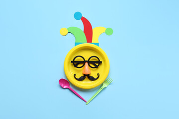 Table setting with funny glasses and paper clown hat for April Fools Day on blue background