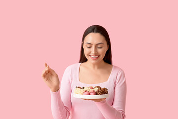 Beautiful young woman holding plate with chocolate covered strawberries on pink background