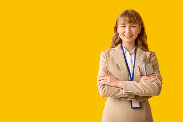 Beautiful young happy female reporter with microphone and badge on yellow background