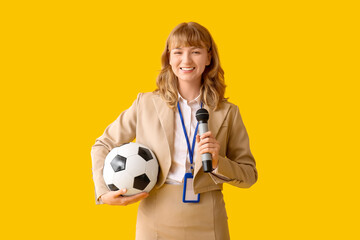 Beautiful young happy female reporter with microphone and soccer ball on yellow background