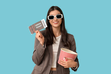 Young woman in 3D cinema eyeglasses with popcorn bucket and ticket on blue background