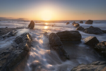 Fototapeta premium Sunset on Barrika beach, Bizkaia with the waves of the Cantabrian Sea breaking between the rocks