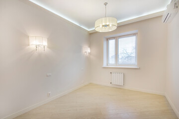 An empty room without furniture with light laminate and walls. Wall lamps and a chandelier on a high ceiling.