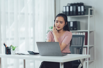 Fototapeta premium Focused & Determined: A young businesswoman works diligently at her desk, her expression focused as she navigates a challenging task on her laptop.
