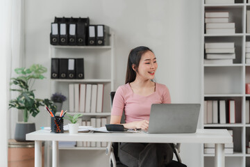 Focused and Engaged: A young businesswoman with a headset,  radiates confidence as she works on her laptop,  surrounded by a tidy and organized office environment.