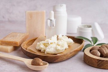 Composition with plate of shea butter, nuts and cosmetic products on light background