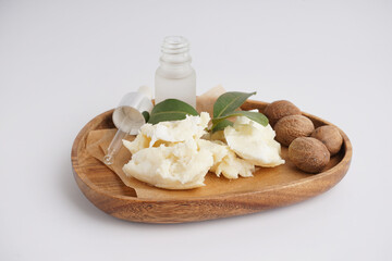 Wooden plate with shea butter, nuts and essential oil on light background