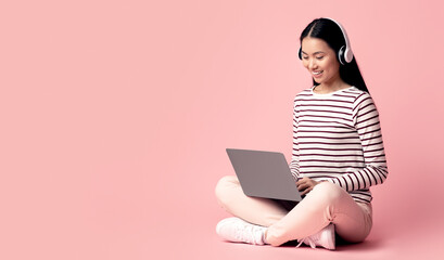 Online Education. Young Asian Woman Study With Laptop And Wireless Headphones While Sitting On Floor Over Pink Studio Background, Happy Korean Female Student Enjoying Distance Learning, Copy Space