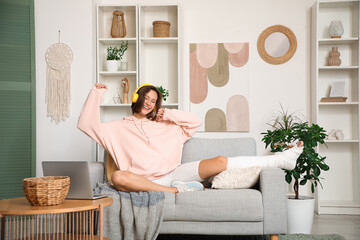 Young woman in headphones with broken leg listening to music on sofa at home