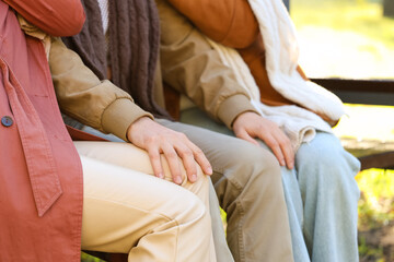 Man with two women sitting on bench in autumn park, closeup. Polyamory concept