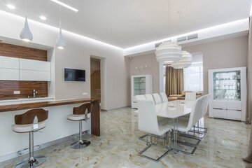 Modern interior of the dining room and kitchen with light floor tiles and white furniture.