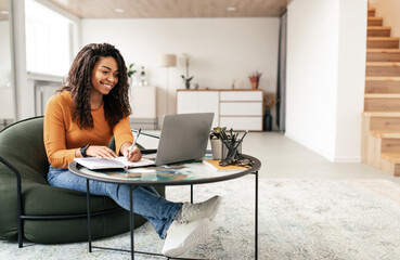 Online Training Concept. Smiling casual black lady sitting at tea coffee table working on pc laptop...