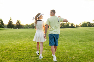 Obraz premium young sports couple in uniform playing golf together on field with lawn at sunset, woman with instructor practicing golf competitions and having active recreation