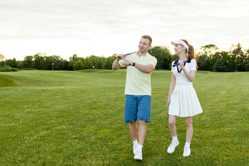Obraz premium young sports couple in uniform playing golf together on field with lawn at sunset, woman with instructor practicing golf competitions and talking