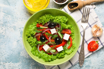 Bowl of tasty Greek salad, fork, spices and oil on color grunge background
