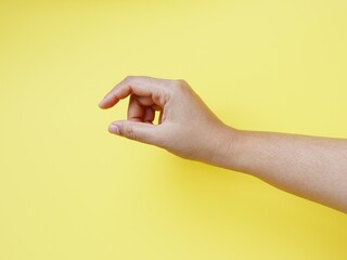 Hand holding a little bit of something, isolated on yellow background. Gesture indicating a pinch...