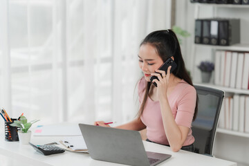 Focused Businesswoman on a Call: A young Asian businesswoman sits at her desk, deeply engrossed in...