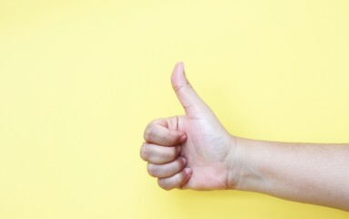 Hand of woman showing thumb-up gesture on yellow background.