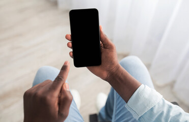 Customer choice, good offer in mobile app. Millennial african american guy disabled in wheelchair holds smartphone with empty screen and going to press finger on screen in living room interior, pov