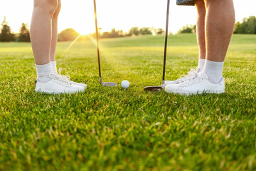 young sports couple in uniform playing golf on the course with clubs and ball on green grass,...