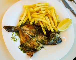 Baked in oven dorado fish with potatoes served with lemon on plate