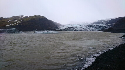 Solheimajokull, Iceland - 3.26.2018: The rapidly melting glacier due to climate change under a cloudy sky with water and icebergs flowing towards the ocean before the pandemic