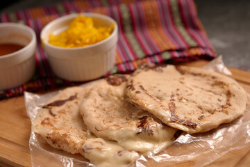Cheese-filled pupusas served with curtido and sauce on a rustic wooden surface, complemented by a vibrant Salvadoran handkerchief.