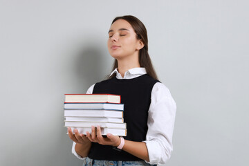 Young student with stack of books on grey background