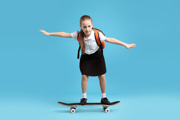 Fototapeta premium Little girl standing on skateboard against light blue background