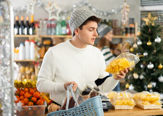 Young guy buyer chooses crispy chips in christmas decorated grocery store