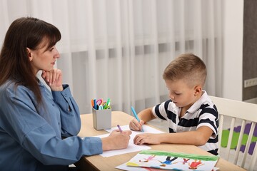 Autism therapy. Psychologist and little boy drawing pictures at table in mental health center