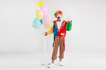 Happy clown with colorful balloons waving on light background