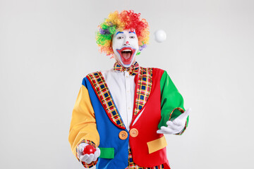 Funny clown juggling balls on light background