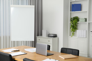 Flip chart, wooden table and chairs in conference room. Mockup for design