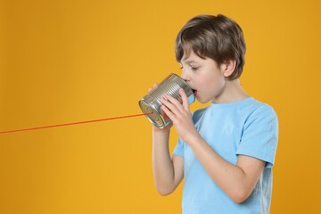 Boy using tin can telephone on orange background