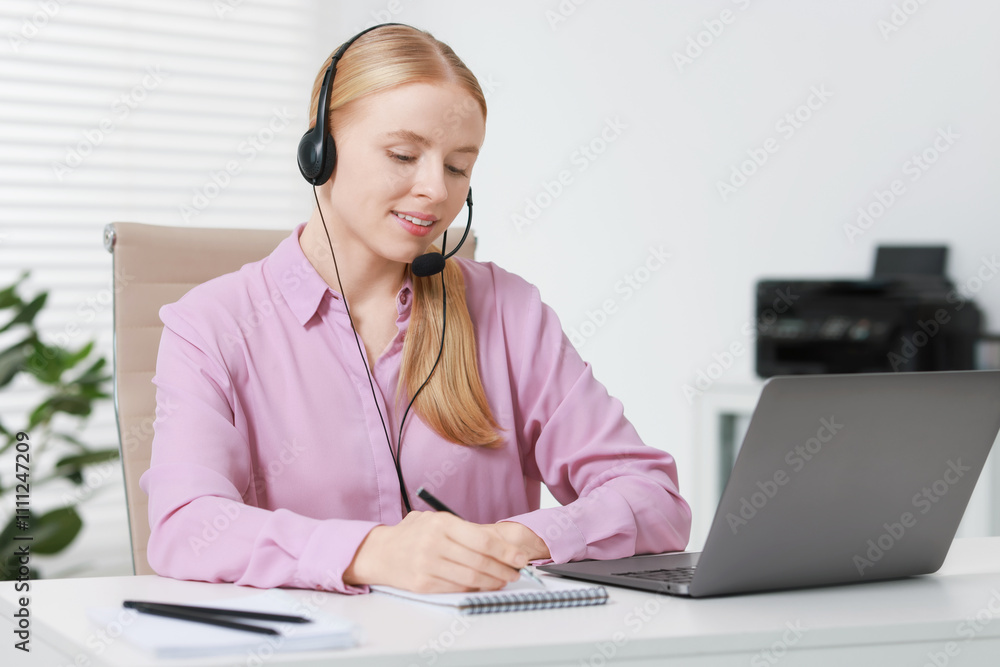 Poster interpreter in headset taking notes while having video chat via laptop at table indoors